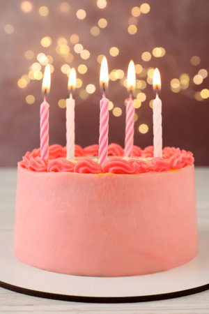 Cute bento cake with tasty cream and burning candles on white wooden tableの写真素材