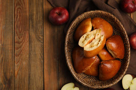 Delicious baked apple pirozhki in wicker basket and fruits on wooden table, flat lay. Space for textの写真素材