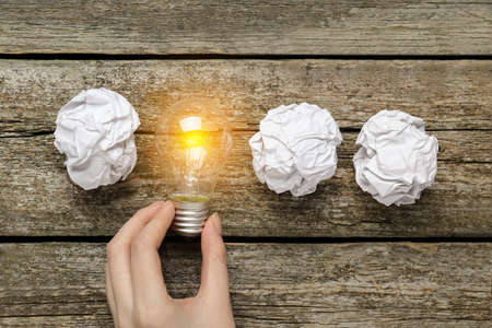 Woman holding lightbulb among paper balls on wooden table, top view. idea conceptの写真素材