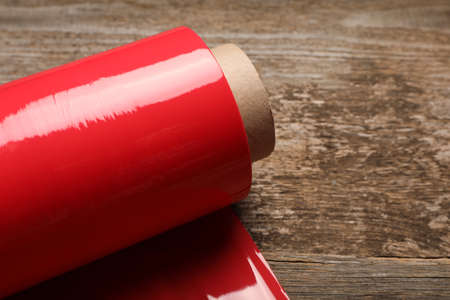 Roll of red plastic stretch wrap on wooden background, closeup. Space for textの写真素材