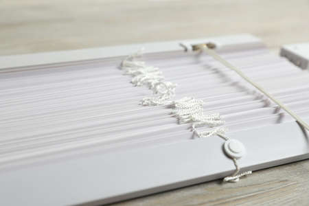 Stylish horizontal window blinds on wooden table, closeup