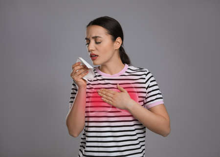 Young woman with tissue coughing on gray background. cold symptomsの写真素材