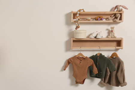 Wooden shelves with baby clothes, toys and accessories on white wall. Space for textの写真素材
