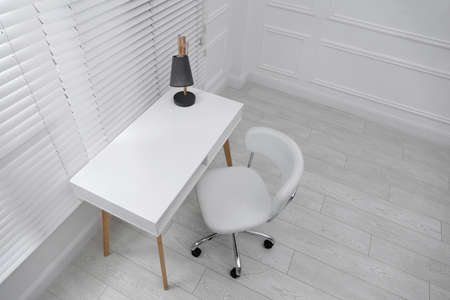 Stylish workplace with white desk and comfortable chair near window indoors. interior designの写真素材