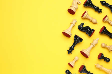 Many different chess pieces on yellow background, flat lay. Space for text