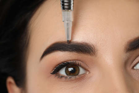 Young woman undergoing procedure of permanent eyebrow makeup in salon, closeup