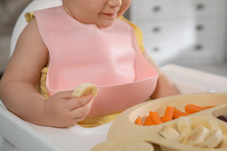 Cute little baby wearing bib while eating at home, closeupの写真素材