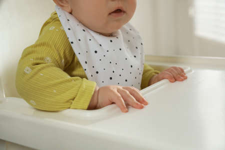 Cute little baby wearing bib in highchair indoors, closeupの写真素材