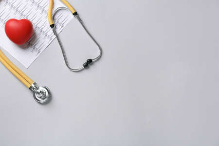 Stethoscope, cardiogram and red decorative heart on gray background, flat lay with space for text....