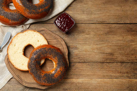 Delicious fresh bagels with poppy seeds and jam on wooden table, flat lay. Space for textの写真素材