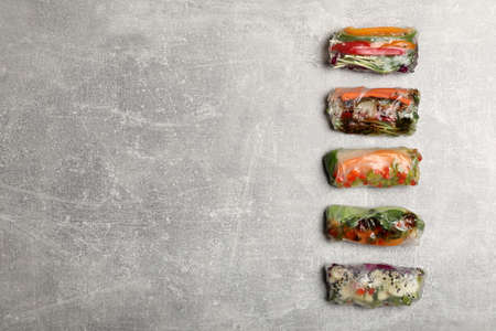 Many different delicious rolls wrapped in rice paper on gray table, flat lay. Space for text