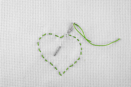 Canvas with embroidered heart and needle as background, top viewの写真素材