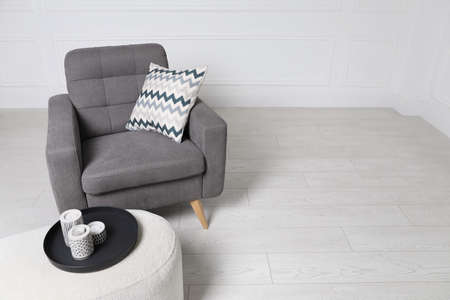 Stylish gray armchair and pouf with candles in the room. interior design