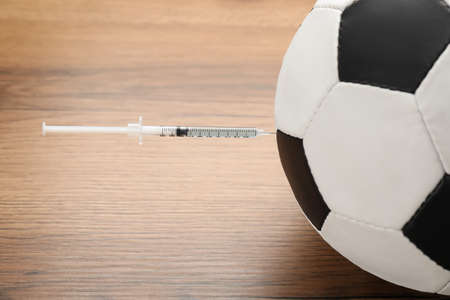 Soccer ball with syringe on wooden table, closeup. Doping conceptの写真素材
