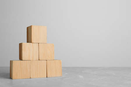 Pyramid of blank wooden cubes on gray table against light background. Space for textの写真素材