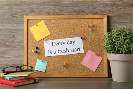 Cork board with motivational quote Every Day is a Fresh Start, stationery and plant on wooden table