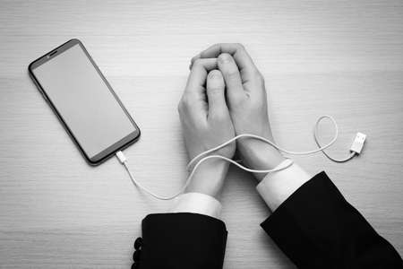 Top view of woman with her hands tangled in charging cable of smartphone at wooden table, black and...