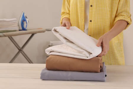 Woman with clean bed linens at white wooden table in laundry room, closeup