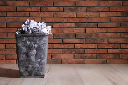 Trash bin full of paper on floor near brick wall, space for text. Recycling rubbish