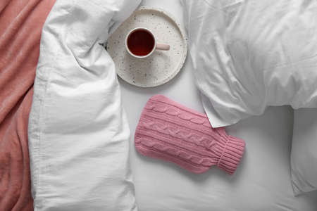 Hot water bottle with knitted cover and cup of tea on bed, flat layの写真素材