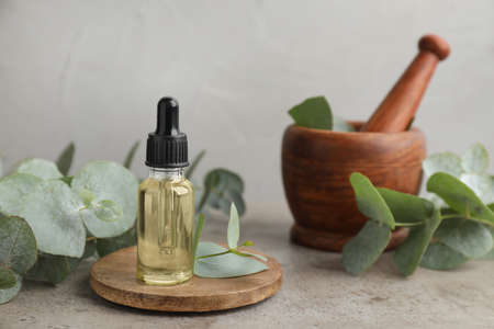 Bottle of eucalyptus essential oil, plant branches, wooden mortar and pestle on gray tableの写真素材