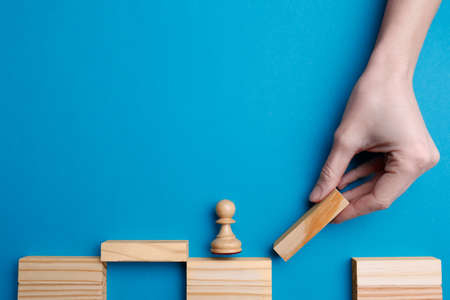 Woman building bridge with wooden blocks on light blue background, top view. Connection and risk...