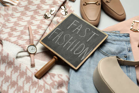 Small chalkboard with phrase FAST FASHION, stylish clothes and accessories on light backgroundの写真素材