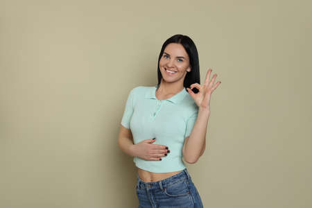 Happy woman touching her belly and showing okay gesture on beige background. concept of healthy...
