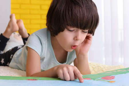 Cute little boy reading book on bed at home, closeupの写真素材
