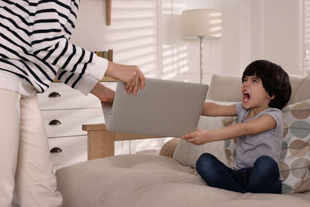 internet addiction. Woman taking laptop from her angry son in living room