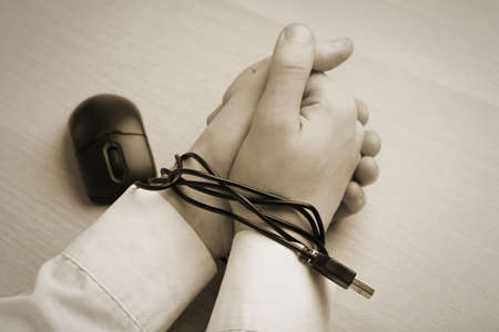 Closeup view of woman with her hands tangled in cable of computer mouse at wooden table, sepia...