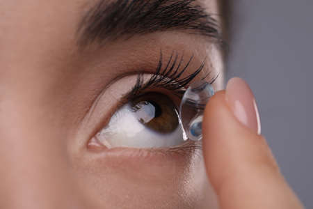 Closeup view of young woman putting in contact lens on gray backgroundの写真素材