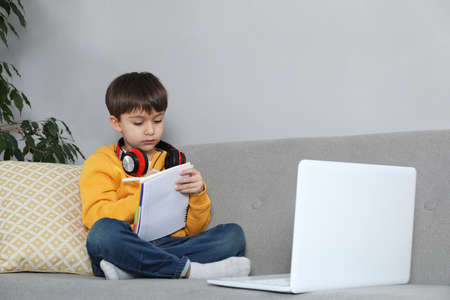Cute little boy with modern laptop studying online at home. e-learning
