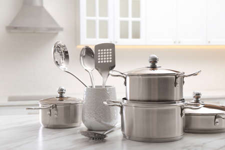 Set of stainless steel cookware and kitchen utensils on white table indoors