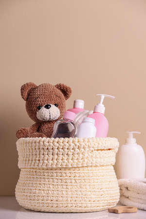 Knitted basket with baby cosmetic products and toy bear on white table against beige backgroundの写真素材