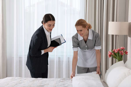 Housekeeping manager with tablet checking maid's work in hotel bedroomの写真素材