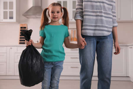 Little girl holding bin bag full of garbage in kitchenの写真素材
