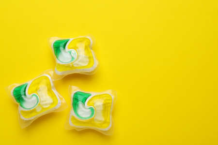 Dishwasher detergent pods on yellow background, flat lay. Space for text