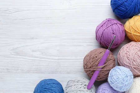 Clews of colorful knitting threads and crochet hook on white wooden table, flat lay. Space for textの写真素材