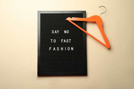 Black letter board with phrase SAY NO TO FAST FASHION, orange hanger on beige background, flat layの写真素材