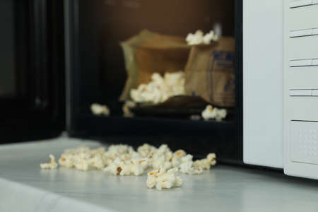 Open microwave oven with fresh popcorn on table, closeup