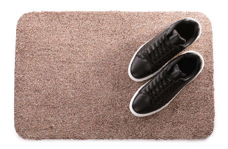 Stylish door mat with shoes on white background, top view