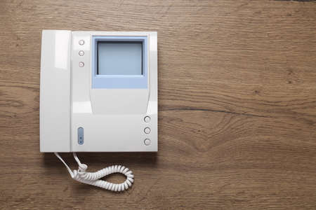 Modern intercom system with handset on wooden background, top view