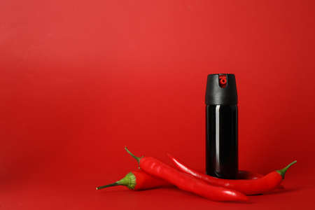 Bottle of gas pepper spray and fresh chili peppers on red background. Space for textの写真素材