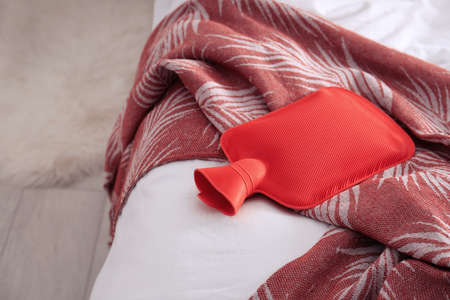 Red hot water bottle on bed indoors