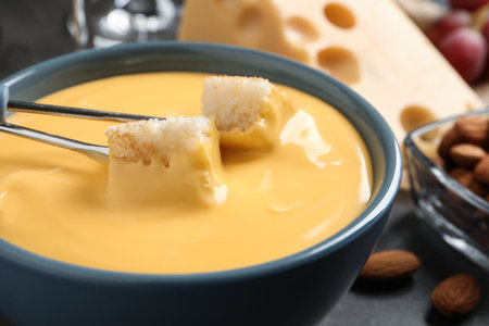 Pot of tasty cheese fondue and forks with bread pieces on gray table, closeup