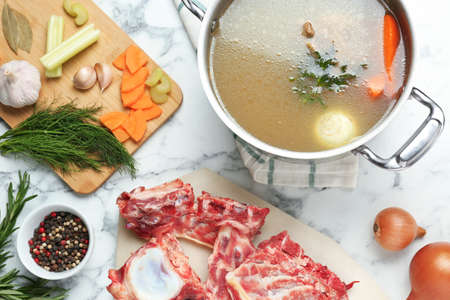 Delicious homemade bone broth and ingredients on white marble table, flat layの写真素材