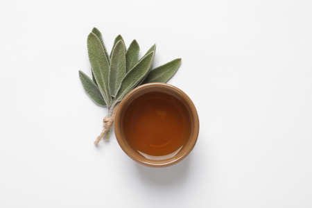 Bowl of essential sage oil and twig on white background, top viewの写真素材
