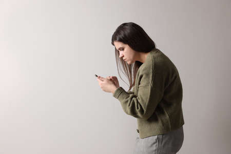 Young woman with bad posture using smartphone on gray background. Space for textの写真素材