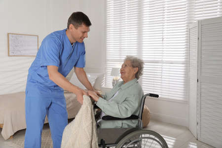 Caregiver assisting senior woman in wheelchair indoors. home health care service